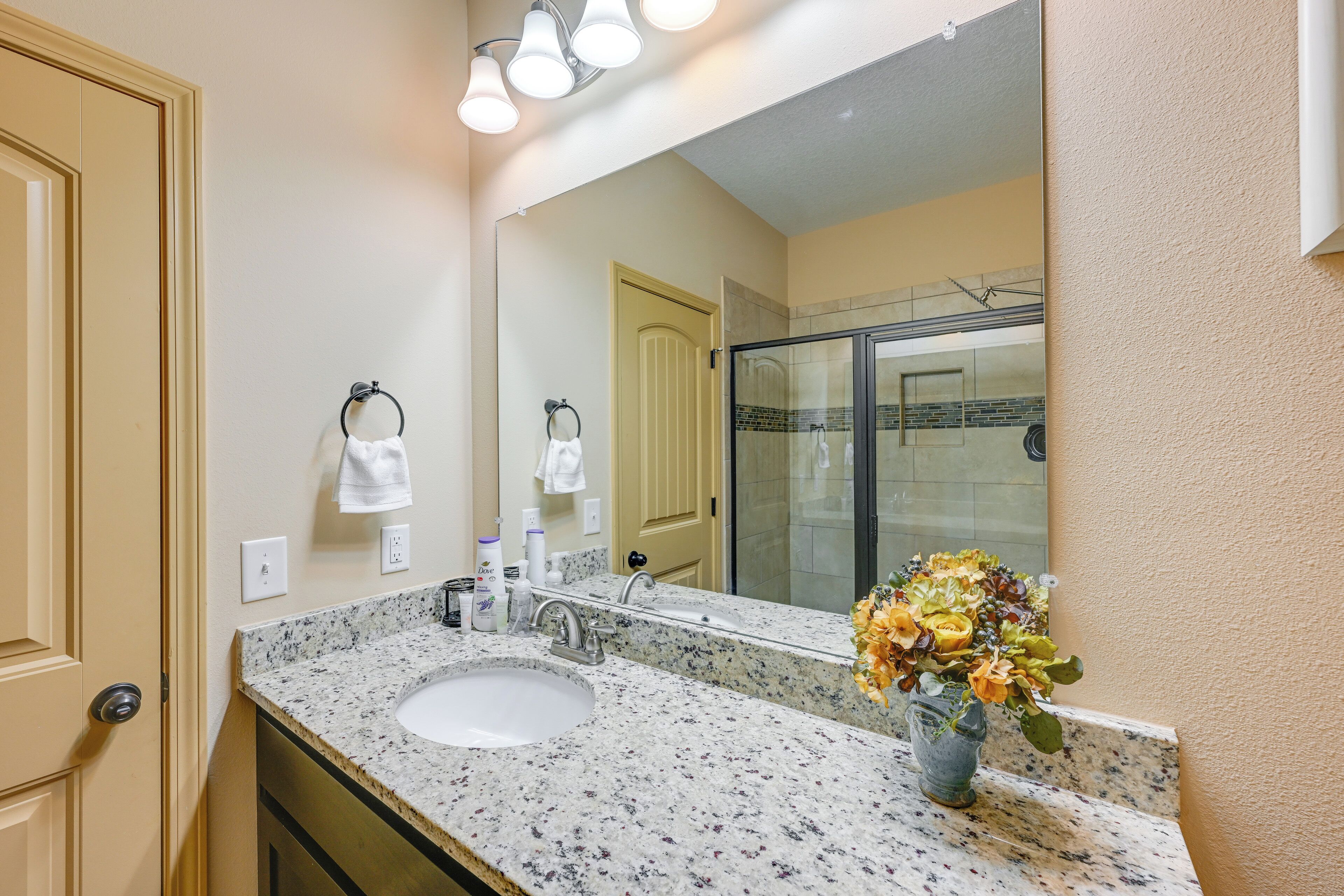 A bathroom with a granite countertop sink, a large mirror, and a shower area.