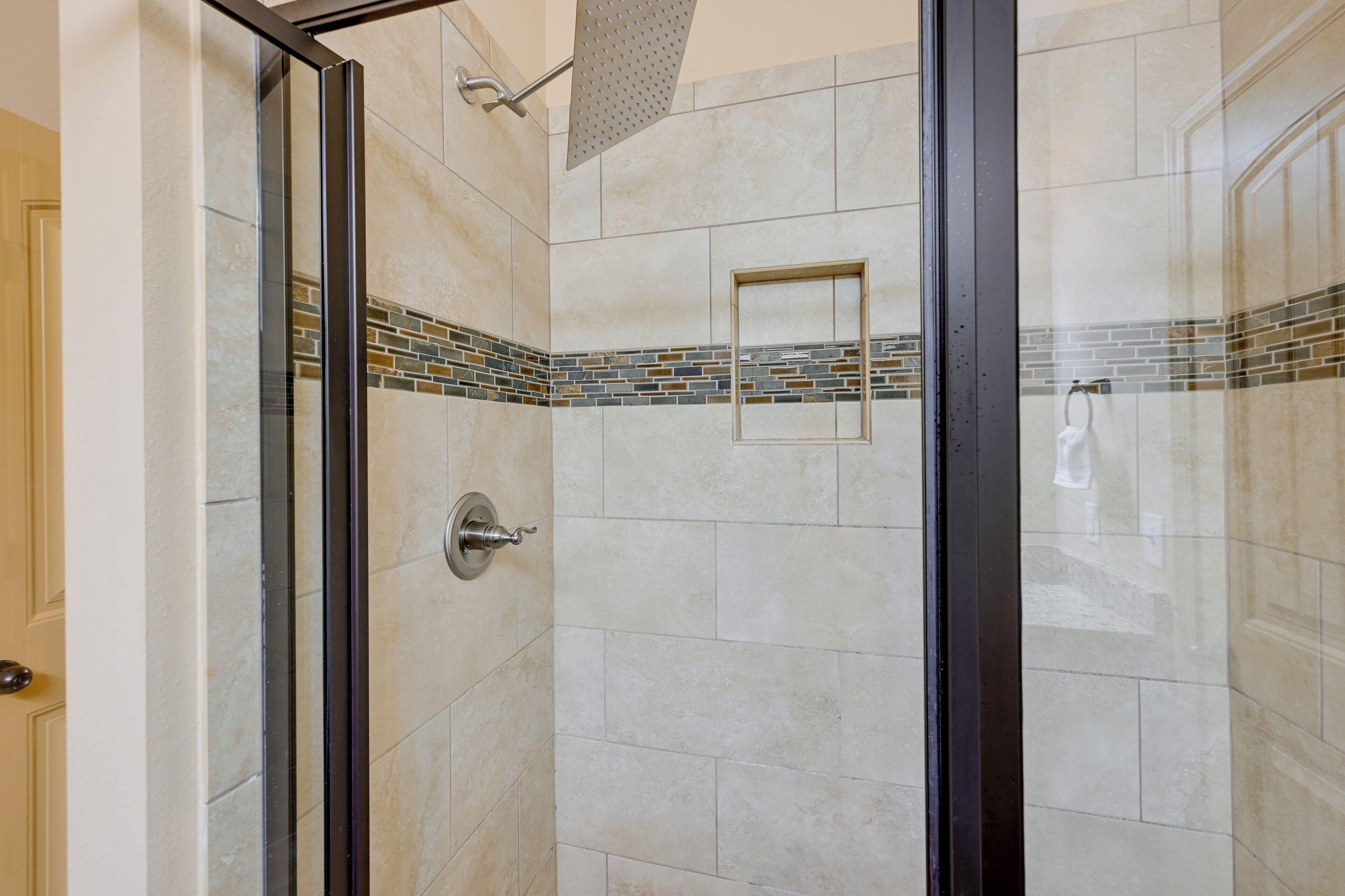 A glass-enclosed shower with a tiled wall, a showerhead, and a towel rack.