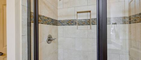 A glass-enclosed shower with a tiled wall, a showerhead, and a towel rack.