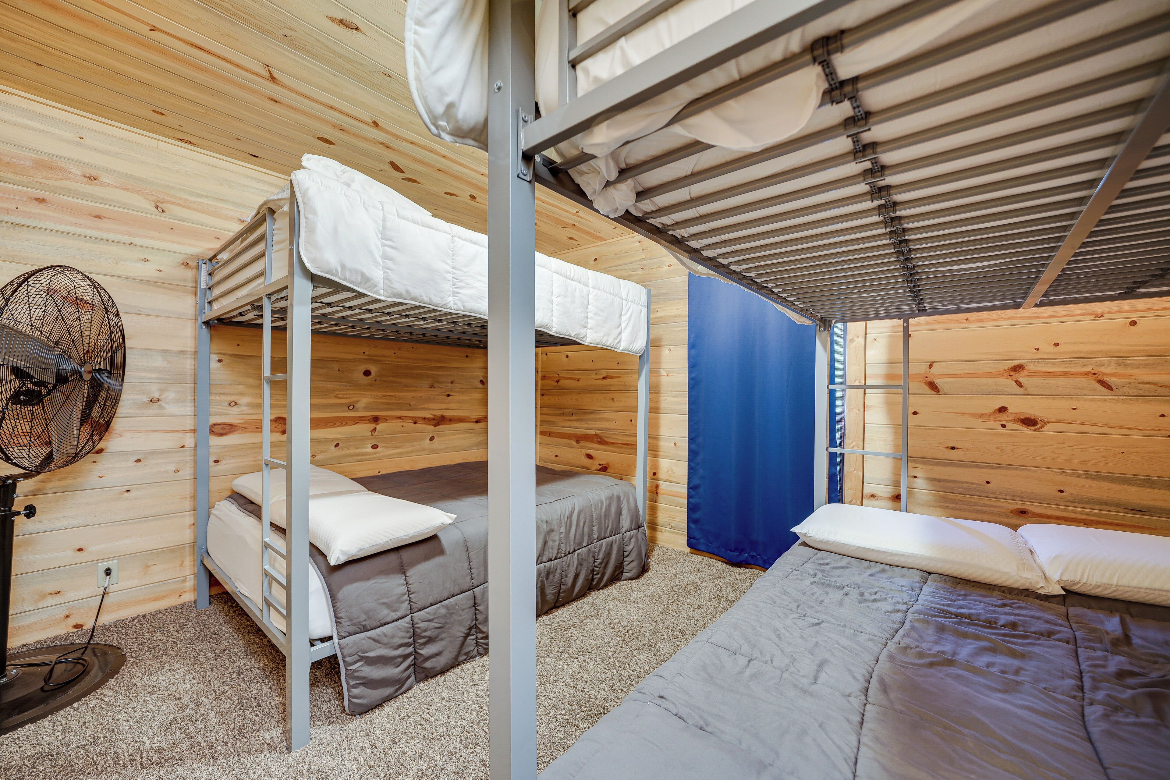 A room with bunk beds, a fan, and a blue curtain.