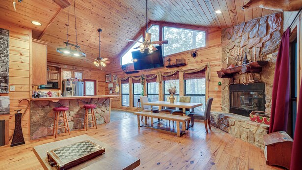 A wooden cabin interior with a stone fireplace, wooden dining table, and a chessboard. - Fort Towson Cabin < 1 Block to Raymond Gary Lake (Fort Towson)