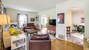 A living room with a sofa, coffee table, and TV. There is a dining area with a table and chairs. The room has wooden flooring and white walls. - Family-friendly Jackson Home w/ Sunroom: Near Golf (Jackson)