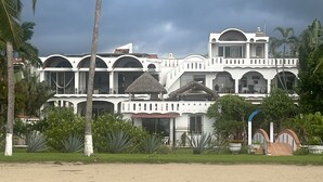 A large, white building with multiple balconies and a thatched-roof structure in front.