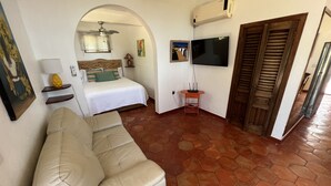 A hotel room with a bed, a sofa, a TV, an air conditioner, and a tiled floor.