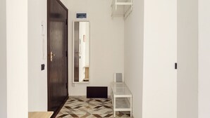 Un couloir avec une porte en bois, une étagère blanche, un miroir et un sol à motifs.