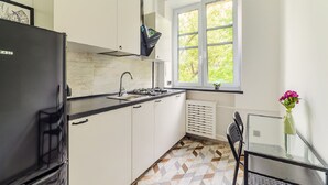 Une cuisine compacte avec un réfrigérateur noir, des armoires blanches, une cuisinière à gaz et une fenêtre donnant sur un paysage verdoyant.