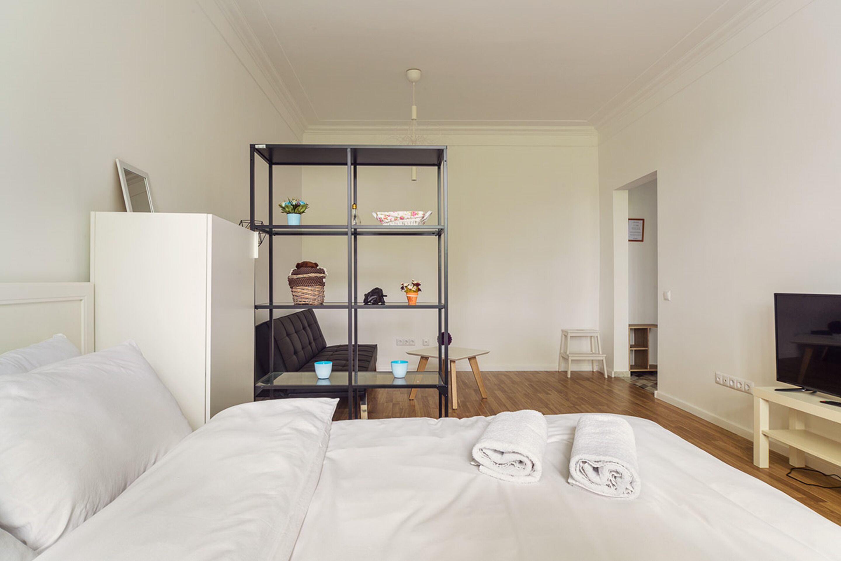 A hotel room with a bed, a TV, a small table, and a bookshelf.