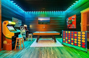A room with a pool table, arcade games, and a pinball machine.