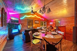 A wooden cabin interior with a dining area, a fireplace, and a ceiling fan.