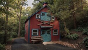 Une cabane rouge avec une porte et des fenêtres bleues, un banc à l’extérieur et un chemin qui y mène.