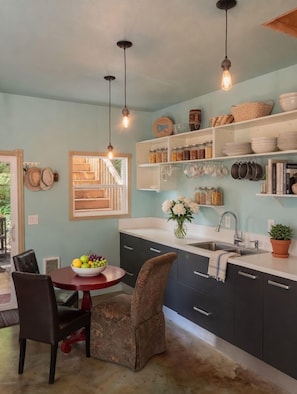 A kitchen with dark cabinets, white countertops, hanging light fixtures, and a dining area with a round table and chairs. - The "Old Barn" in the woods. Peace, Romance, Ahhh (Portland)