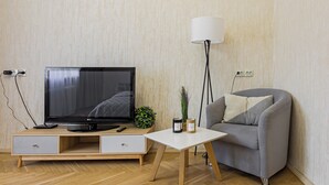 Un soggiorno moderno con una TV a schermo piatto, un divano grigio, un tavolino da caffè bianco e una lampada da terra.