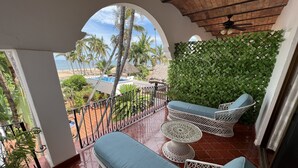 Un balcon donnant sur la plage, un toit de chaume et une balustrade blanche.