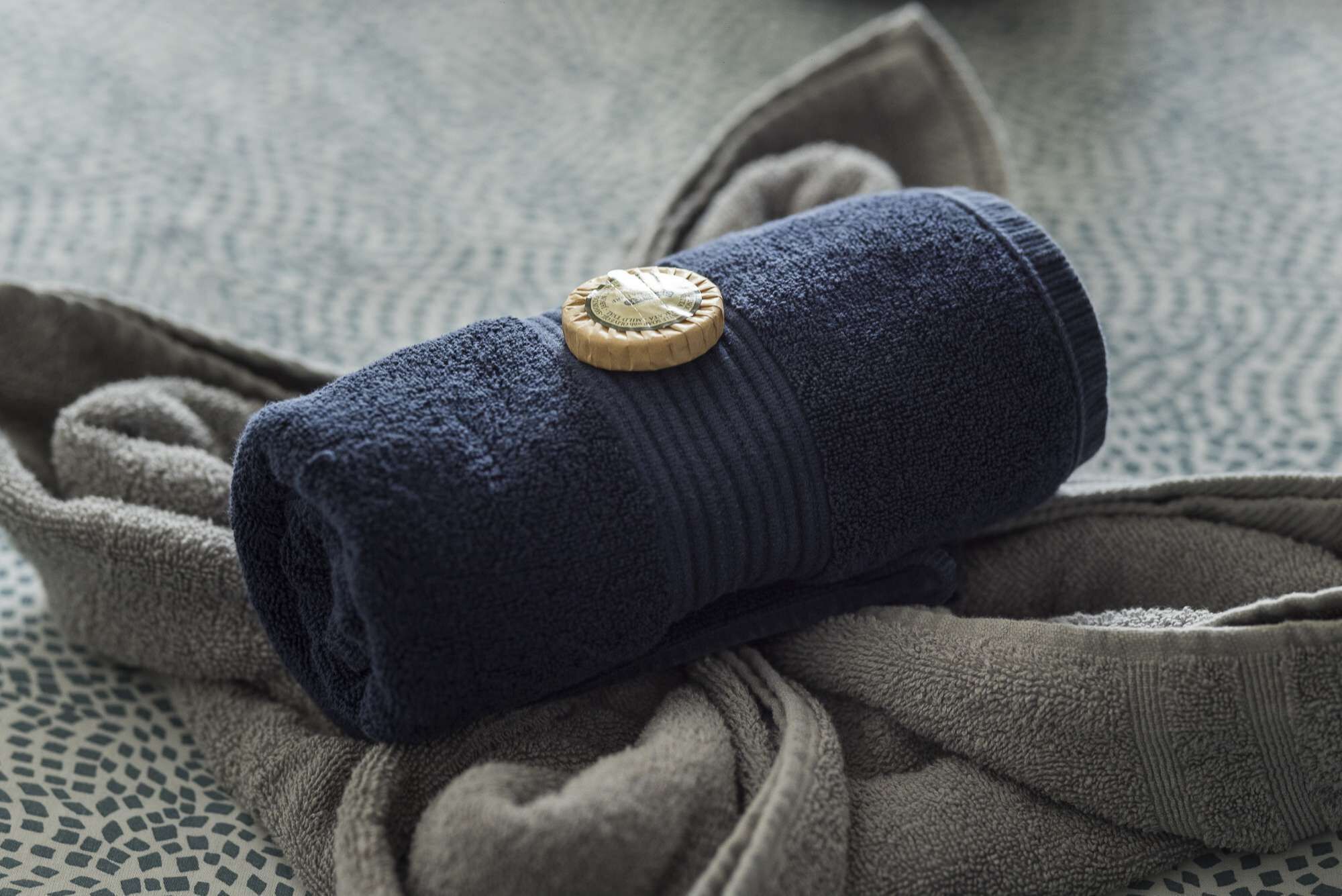 A rolled-up dark blue towel with a wooden button, placed on a textured fabric surface.