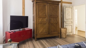 Ett rum med en garderob i trä, ett rött skåp med en tv och en korg av rotting.