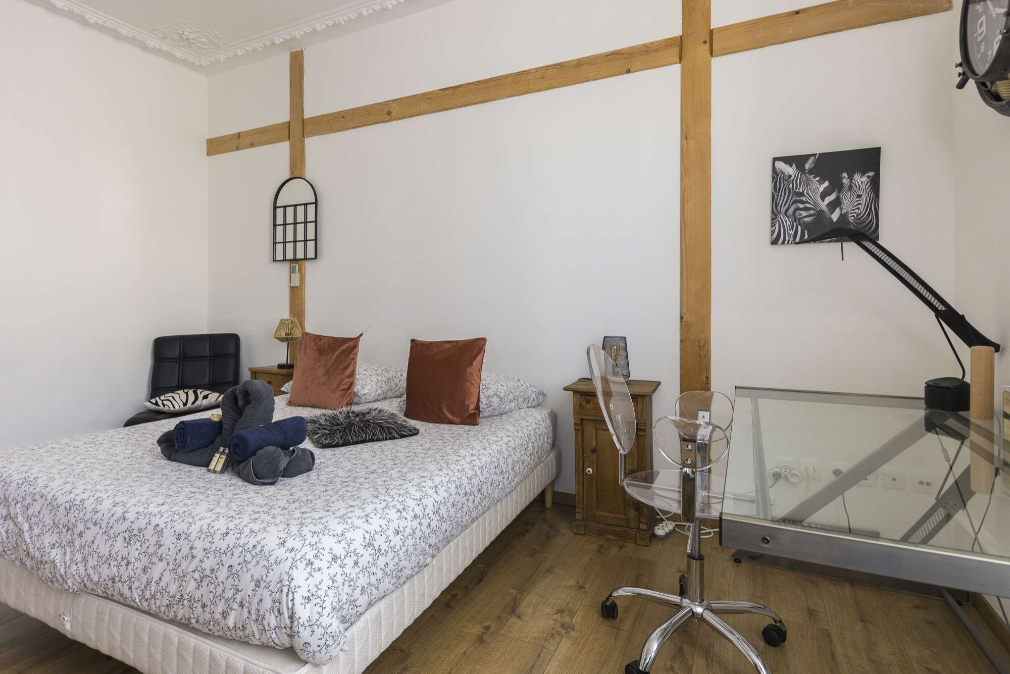 Un dormitorio con cama, escritorio con silla, un reloj de pared y una obra de arte con cebra.