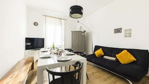 Ett modernt vardagsrum med en matplats, med en soffa med gula kuddar, ett träbord och en tv som är monterad på väggen.
