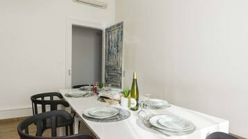Un coin repas avec une table blanche dressée pour quatre personnes, comprenant des assiettes, des couverts et une bouteille de vin.