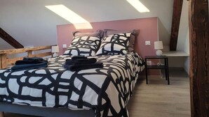 Une chambre à coucher avec un lit, des oreillers, une table de chevet et une structure en poutres apparentes.