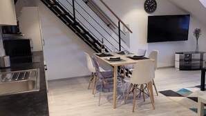Une cuisine moderne dotée d’une cuisinière intégrée, un coin repas avec une table et des chaises, un escalier et un téléviseur à écran plat fixé au mur.