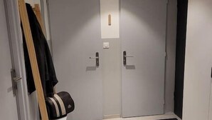 Un couloir avec deux portes, un banc sur lequel se trouve un sac, et un petit tapis sur le sol.