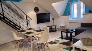 Un salon moderne comprenant un coin repas, un escalier, un téléviseur à écran plat et une grande fenêtre avec des rideaux.