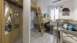A compact living space with a bunk bed, a dining area with a table and chairs, and a kitchen area with a stove and sink. - St Léon Strasbourg - Studio - 3 Pers (STRASBOURG)
