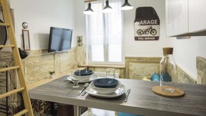 A dining area with a wooden table set for two, a television on the wall, and a sign indicating a garage service. - St Léon Strasbourg - Studio - 3 Pers (STRASBOURG)