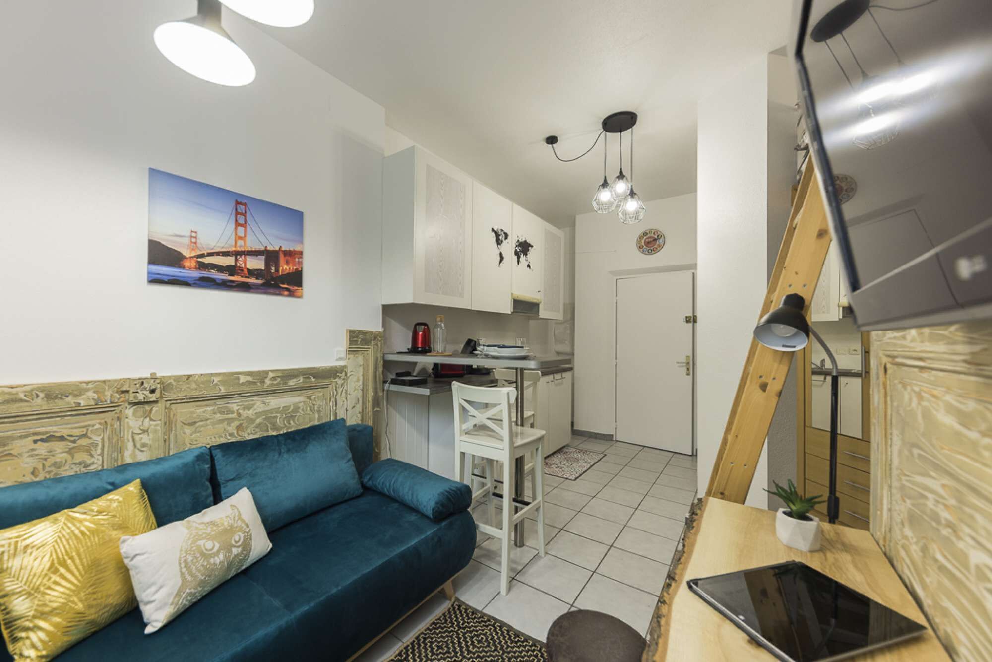 En kompakt opholdsstue med sofa, spisebord, tekøkken og en loftlampe.