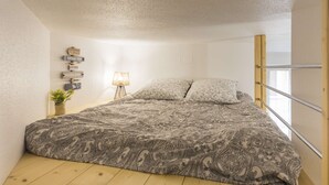 A bedroom with a bed, a nightstand, a lamp, and a wall with signs. - St Léon Strasbourg - Studio - 3 Pers (STRASBOURG)