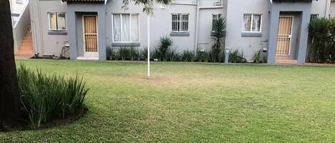 Una propiedad residencial con césped cuidado, un árbol y una casa con tejado de tejas y varias ventanas.