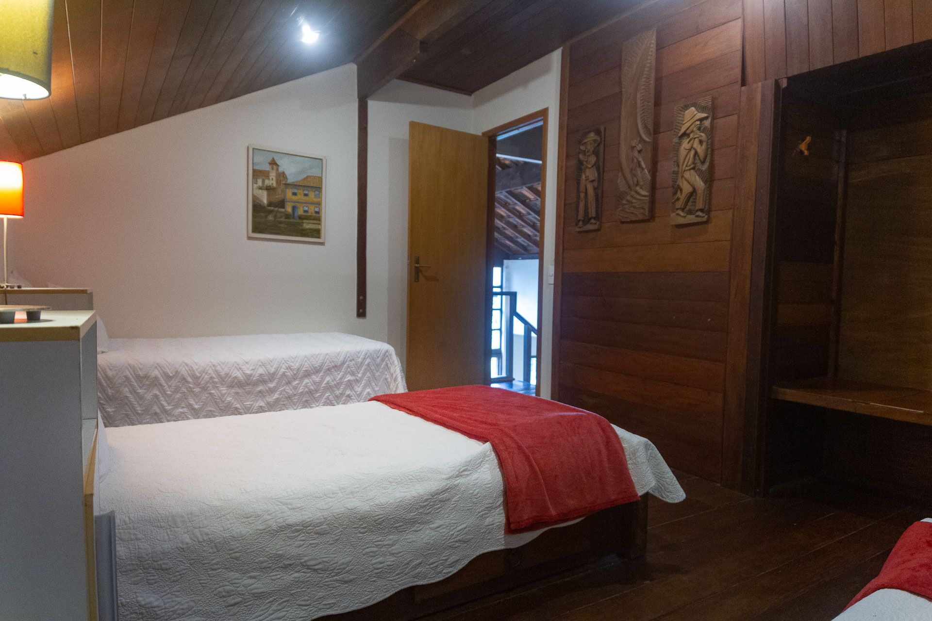 A room with two beds, wooden walls, a painting, and a door leading to a staircase.