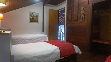 A room with two beds, wooden walls, a painting, and a door leading to a staircase.