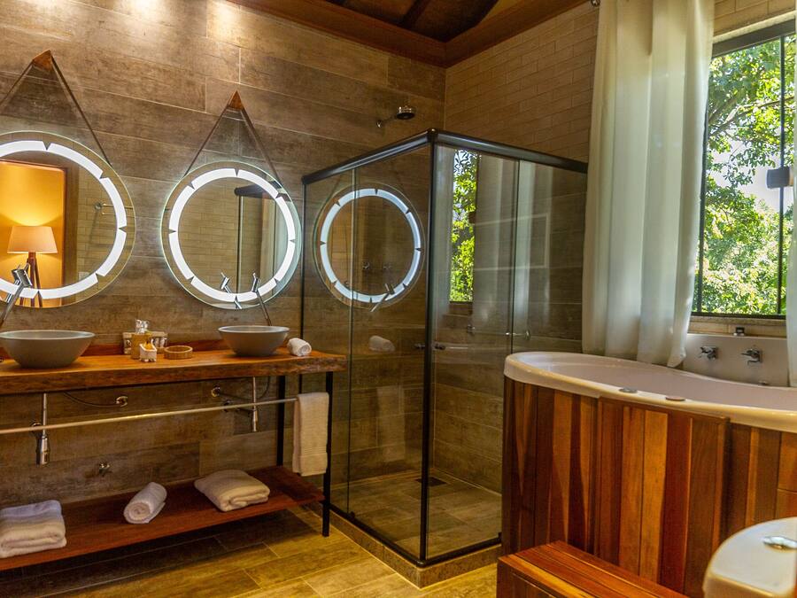 Un baño moderno con tocador de madera, ducha con cerramiento de vidrio y tres espejos iluminados.
