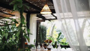 A table set with glassware and a vase of flowers, surrounded by greenery and a hanging light fixture.