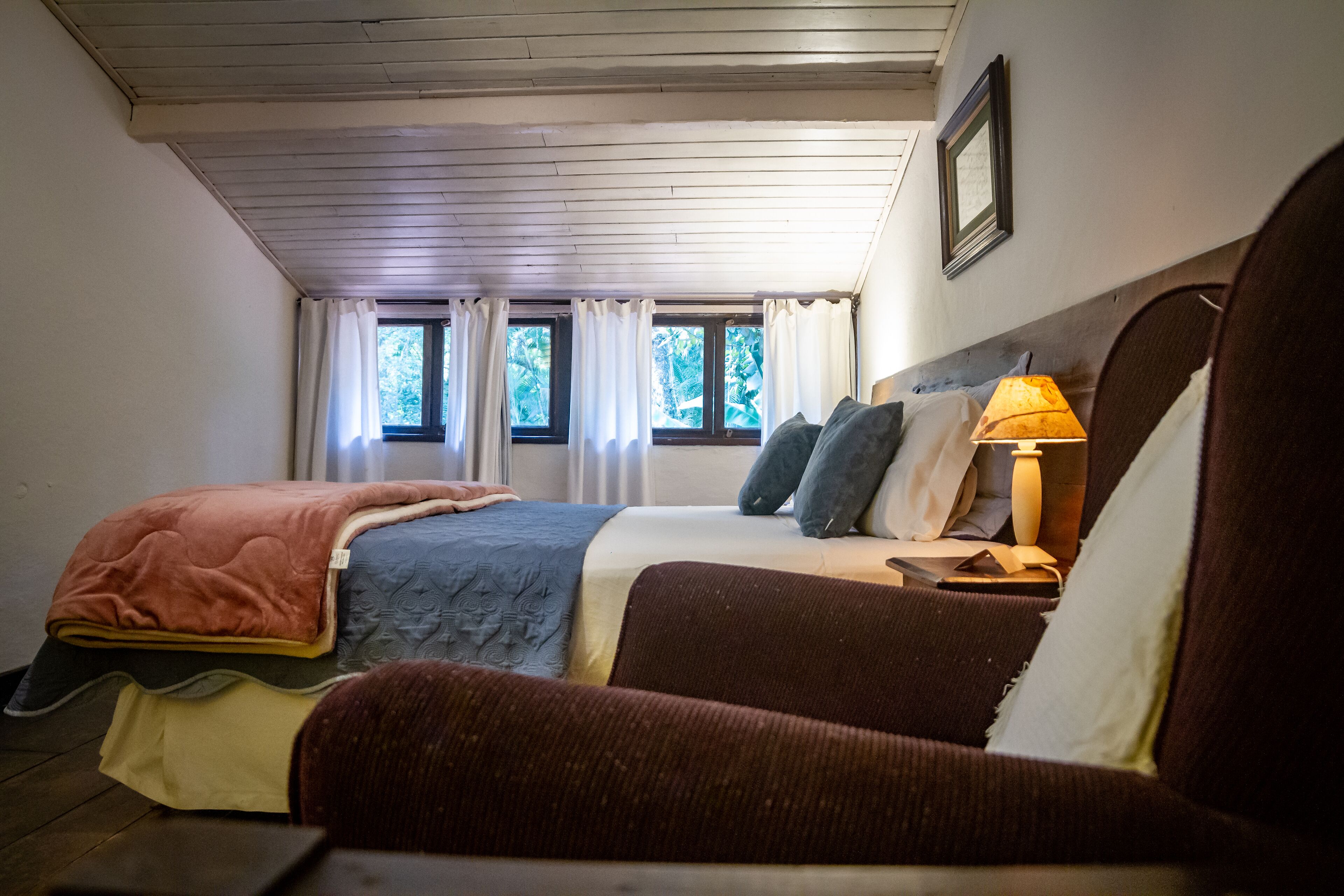 A bedroom with a bed, a chair, a nightstand, a lamp, and a window with curtains.