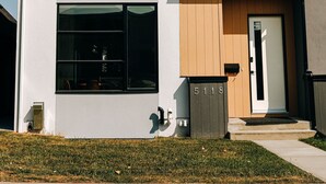 A modern two-story house with a white facade, large windows, and a wooden door. - Luxury Home | Sleeps 8, Fireplace, Prime Location, A/C (Calgary)