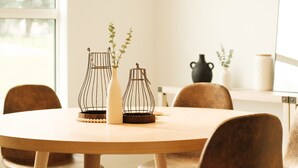 A dining area with a round wooden table, six brown chairs, hanging pendant lights, and decorative vases with plants. - Luxury Home | Sleeps 8, Fireplace, Prime Location, A/C (Calgary)
