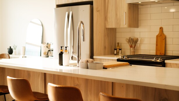 A modern kitchen with a stainless steel refrigerator, a wooden countertop, and three brown bar stools. - Luxury Home | Sleeps 8, Fireplace, Prime Location, A/C (Calgary)