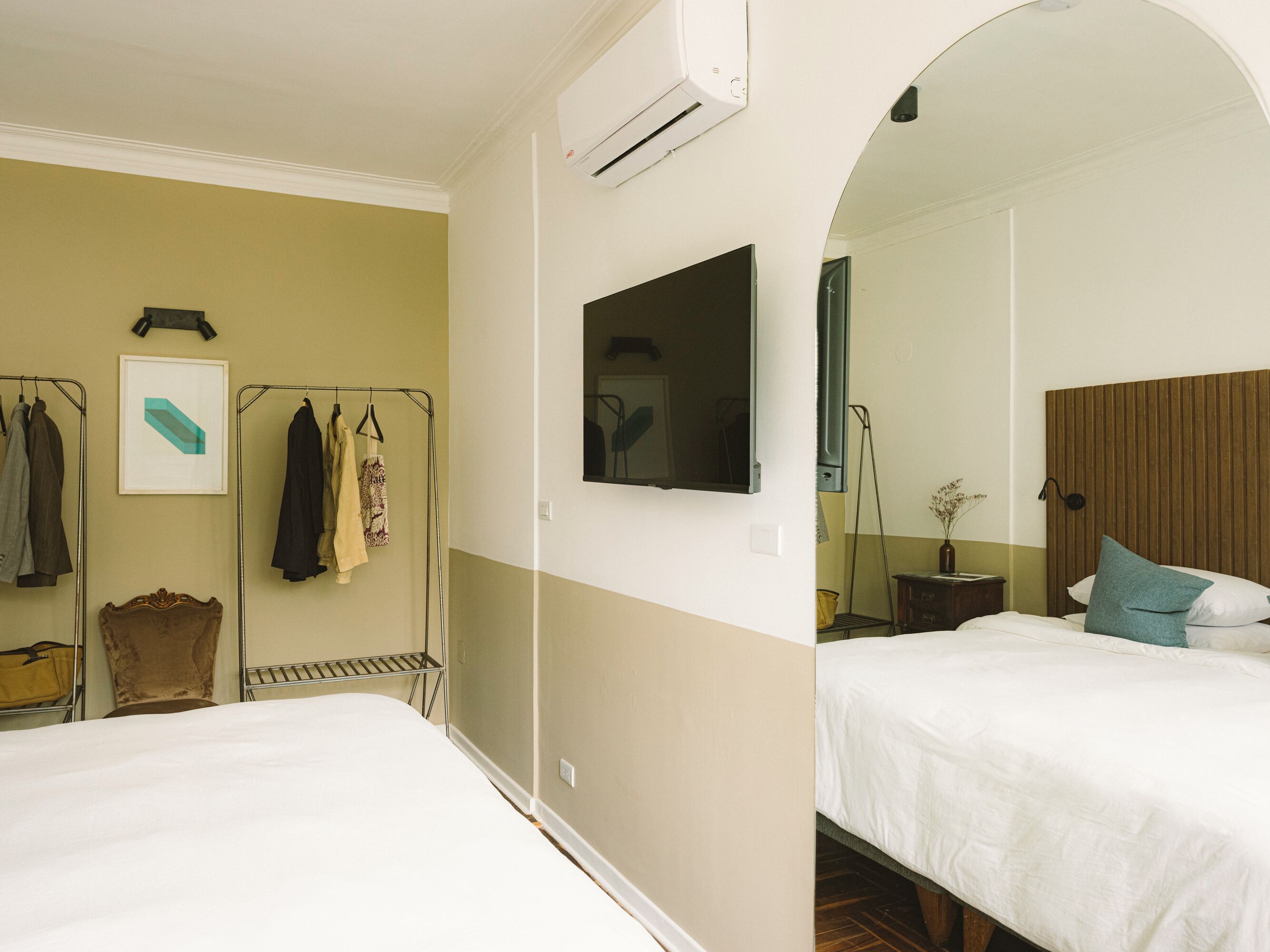 Habitación de hotel con dos camas, un televisor montado, un armario y un espejo.