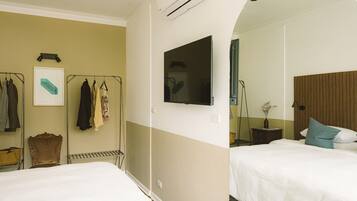 Habitación de hotel con dos camas, un televisor montado, un armario y un espejo.