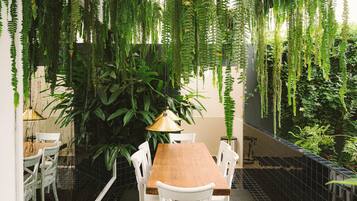 Un comedor con una mesa de madera y sillas blancas, rodeado de helechos colgantes y plantas.