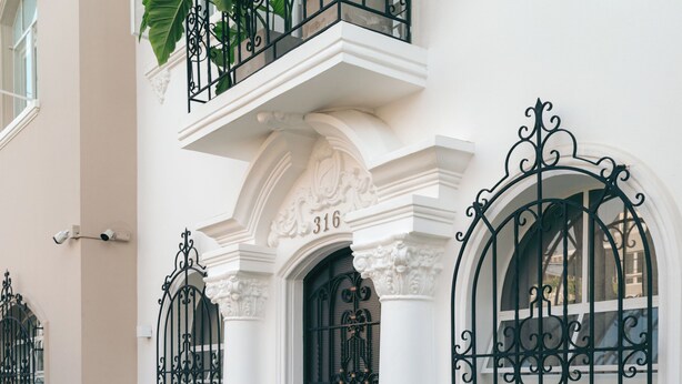 Un edificio con paredes exteriores blancas, rejas negras de hierro forjado y grandes macetas con plantas.