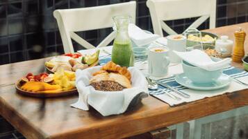 A dining table with a variety of food items, a hanging light fixture, and a view of greenery in the background.