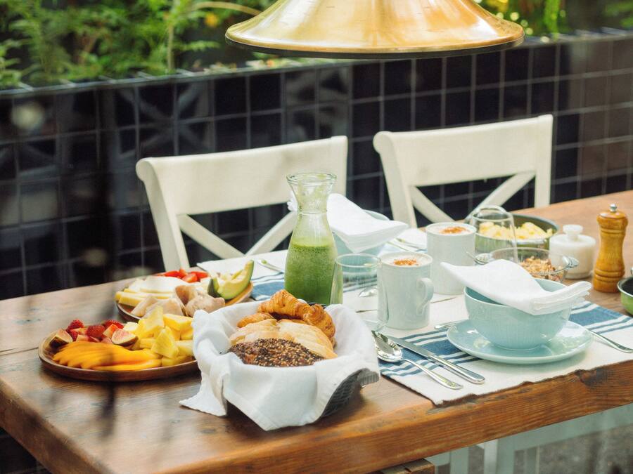 A dining table with a variety of food items, a hanging light fixture, and a view of greenery in the background.