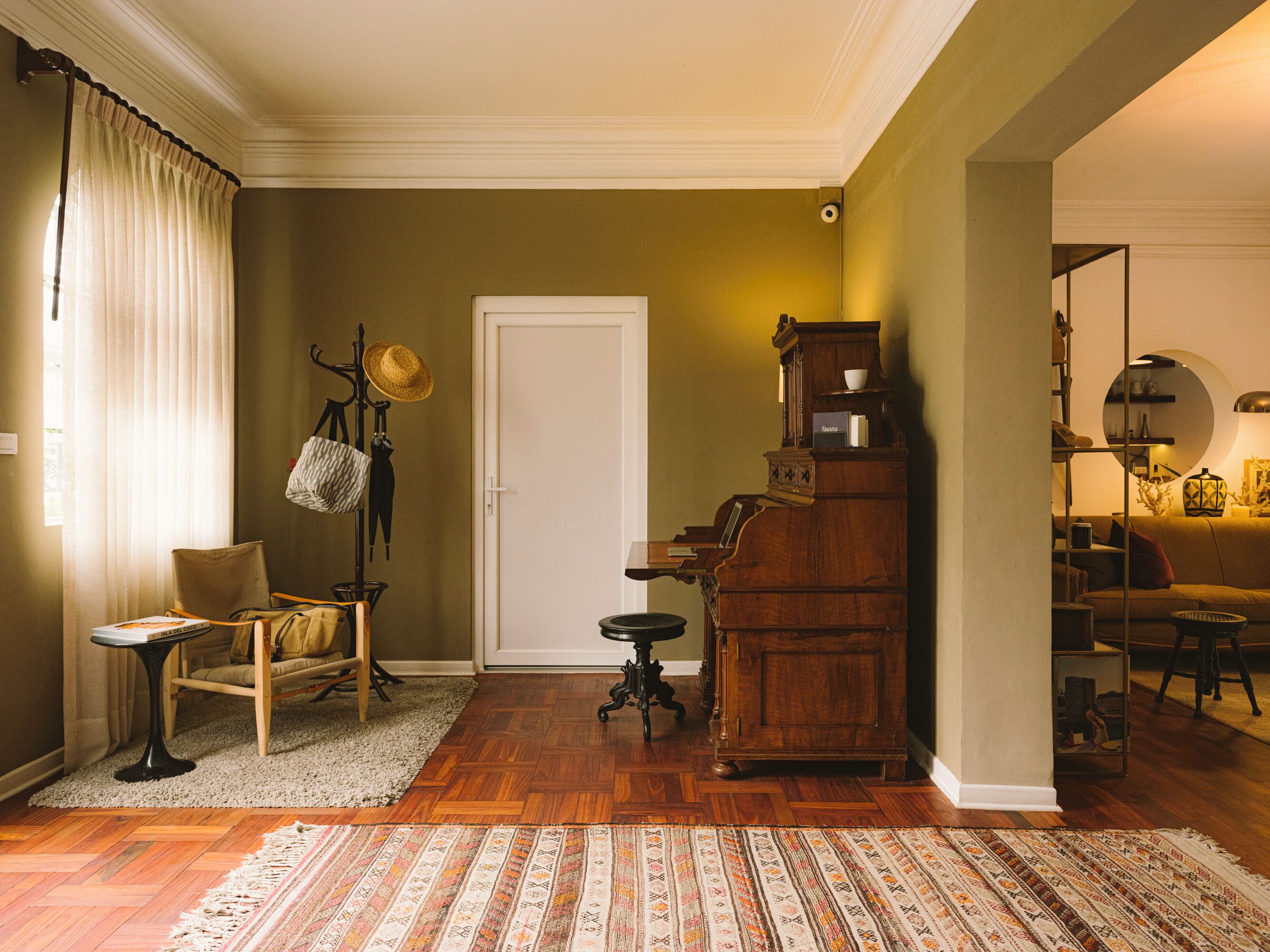 A room with a piano, a chair, a table, and a patterned rug.
