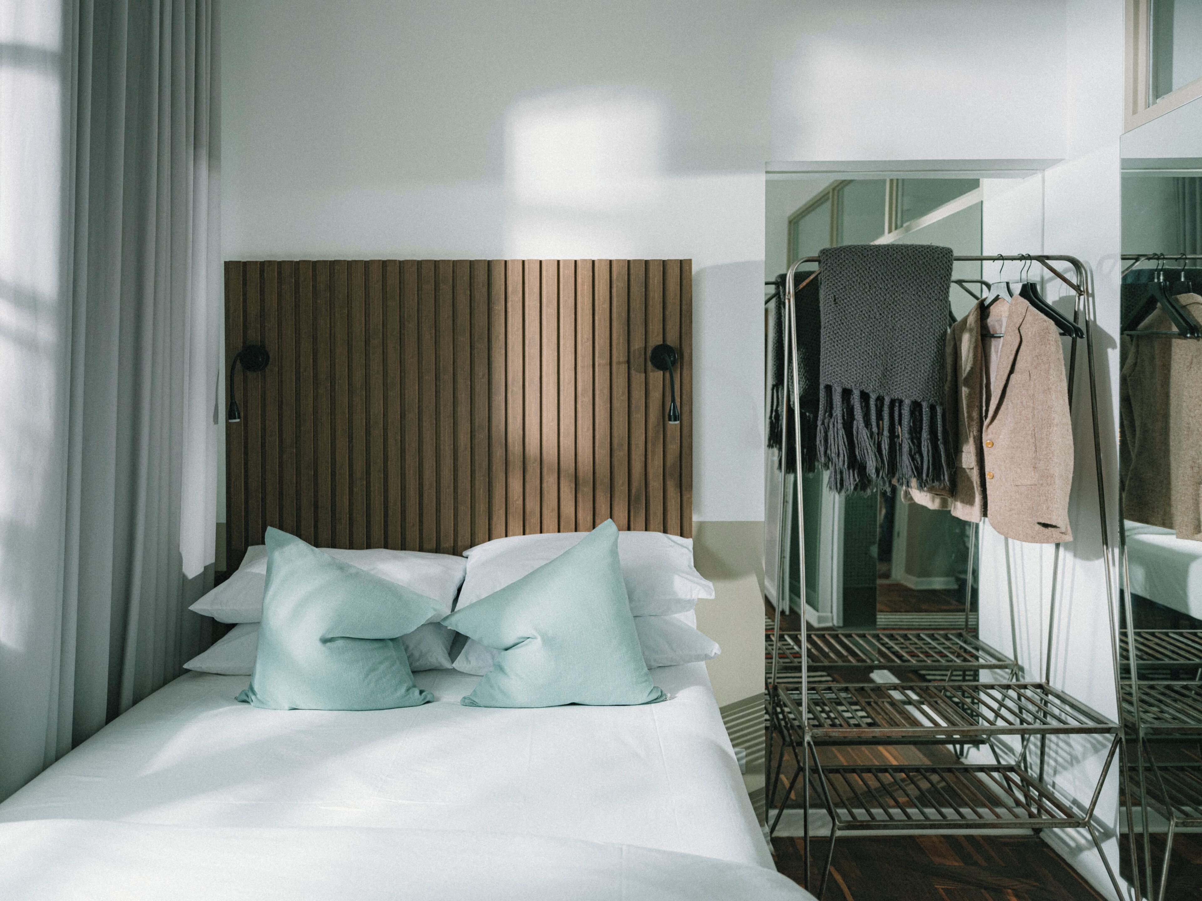 Een hotelkamer met een bed, een houten hoofdeinde, een metalen droogrek en uitzicht op een badkamer.