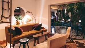 Una sala de estar con sofá, sillón, mesa de centro y lámpara. Se ve una escalera apoyada en la pared y un espejo circular.