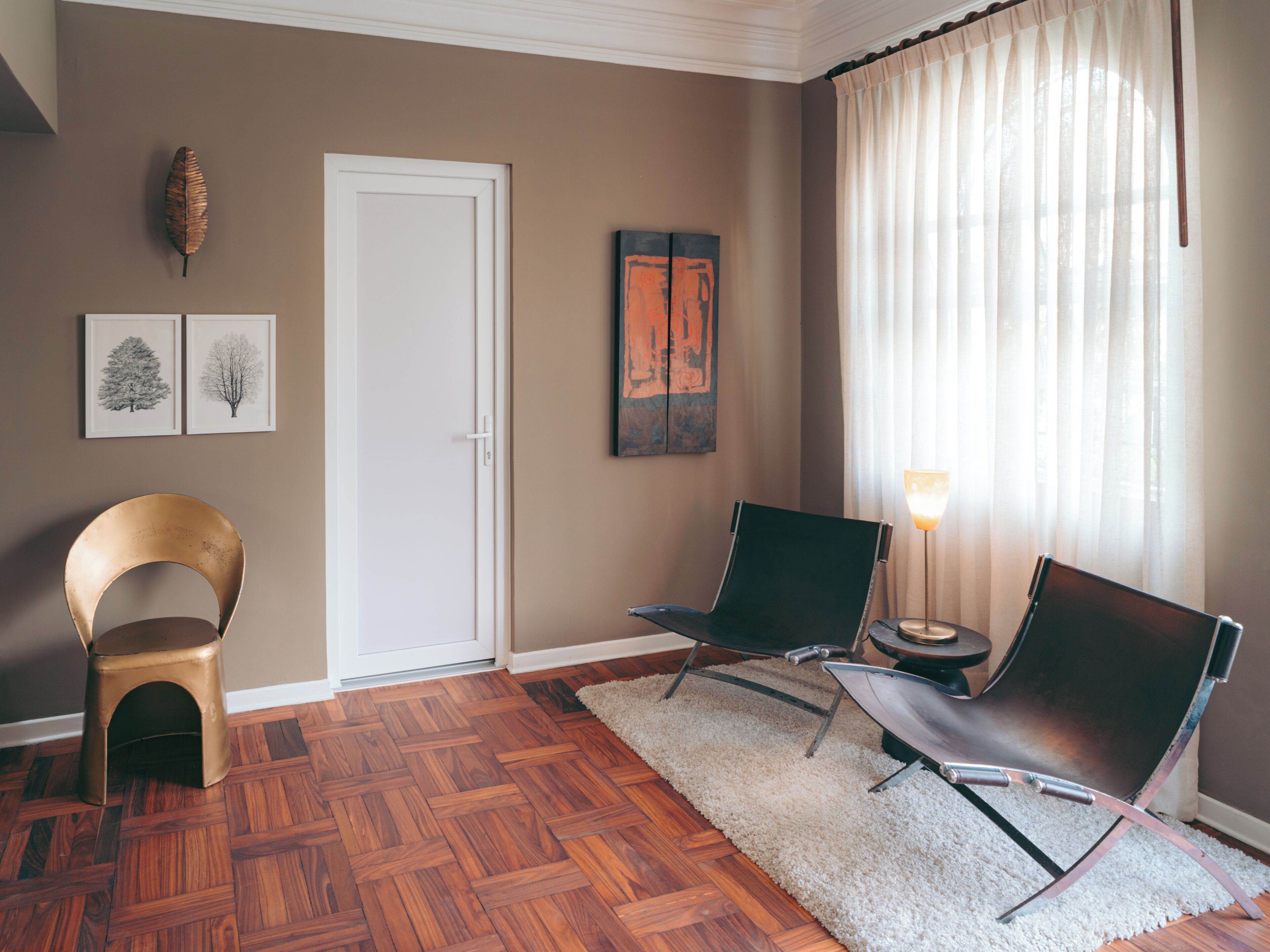 A room with a wooden parquet floor, a white door, two chairs, a small round table, and a lamp.