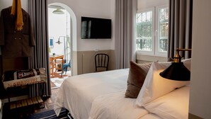 Habitación de hotel con cama, televisor montado en la pared, una silla y una ventana con cortinas.